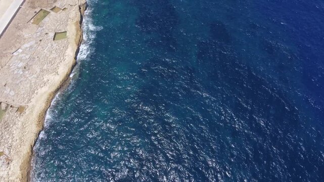 Xwejni s centuries-old salt pans unfold along the rugged coast of Zebbug, Gozo, geometric pools and vivid Mediterranean blues in a sweeping summer Aerial view. High quality 4k footage