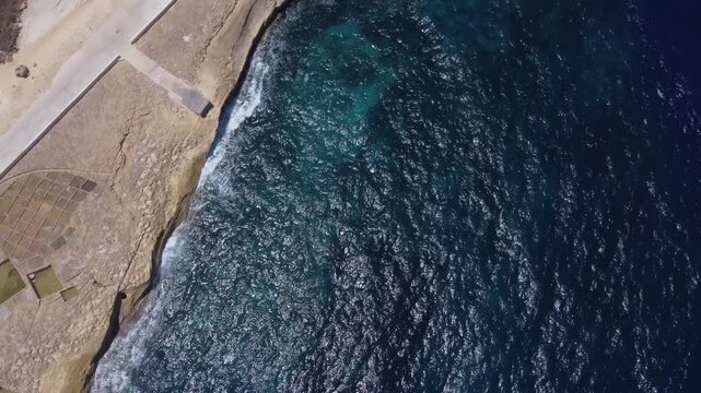 Xwejni s centuries-old salt pans unfold along the rugged coast of Zebbug, Gozo, geometric pools and vivid Mediterranean blues in a sweeping summer Aerial view. High quality 4k footage