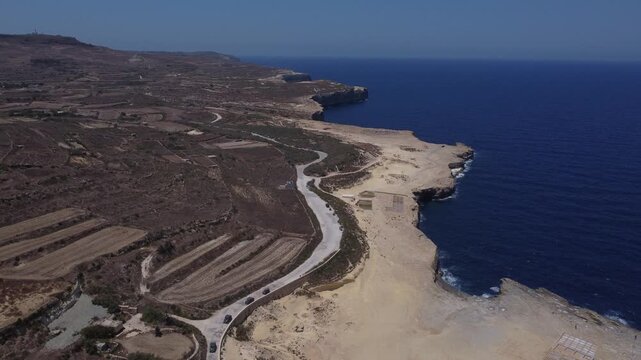 Xwejni s centuries-old salt pans unfold along the rugged coast of Zebbug, Gozo, geometric pools and vivid Mediterranean blues in a sweeping summer Aerial view. High quality 4k footage