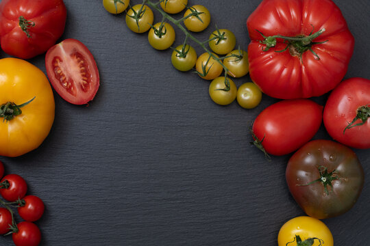A background with a frame made of various tomatoes arranged on a slate slab. There is space in the center for text.
