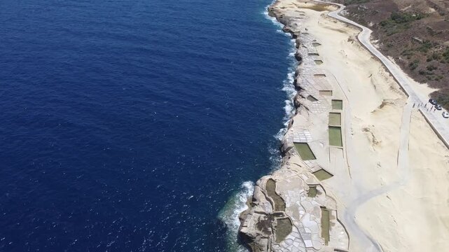 Xwejni s centuries-old salt pans unfold along the rugged coast of Zebbug, Gozo, geometric pools and vivid Mediterranean blues in a sweeping summer Aerial view. High quality 4k footage