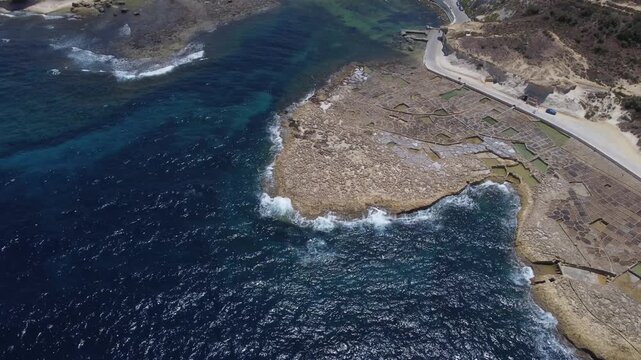 Xwejni s centuries-old salt pans unfold along the rugged coast of Zebbug, Gozo, geometric pools and vivid Mediterranean blues in a sweeping summer Aerial view. High quality 4k footage