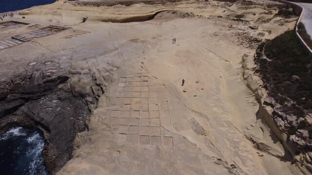 Xwejni s centuries-old salt pans unfold along the rugged coast of Zebbug, Gozo, geometric pools and vivid Mediterranean blues in a sweeping summer Aerial view. High quality 4k footage