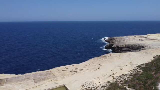 Xwejni s centuries-old salt pans unfold along the rugged coast of Zebbug, Gozo, geometric pools and vivid Mediterranean blues in a sweeping summer Aerial view. High quality 4k footage