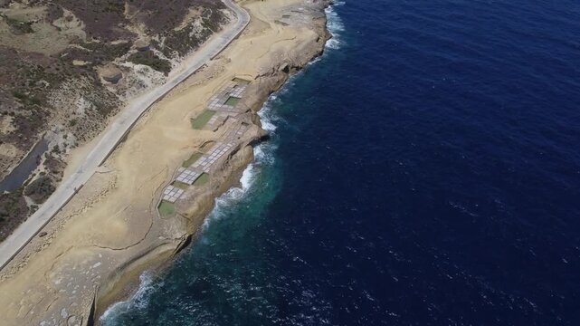 Xwejni s centuries-old salt pans unfold along the rugged coast of Zebbug, Gozo, geometric pools and vivid Mediterranean blues in a sweeping summer Aerial view. High quality 4k footage