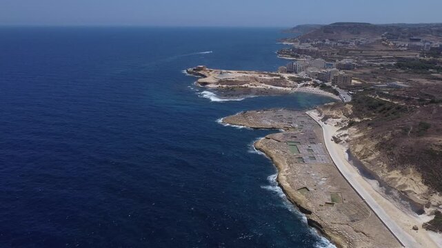 Xwejni s centuries-old salt pans unfold along the rugged coast of Zebbug, Gozo, geometric pools and vivid Mediterranean blues in a sweeping summer Aerial view. High quality 4k footage
