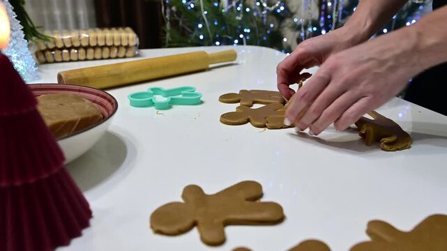 Beautiful girl's hands work expertly with gingerbread dough, shaping charming figures. A colorful Christmas tree glimmers in the background, enhancing the festive spirit of baking.