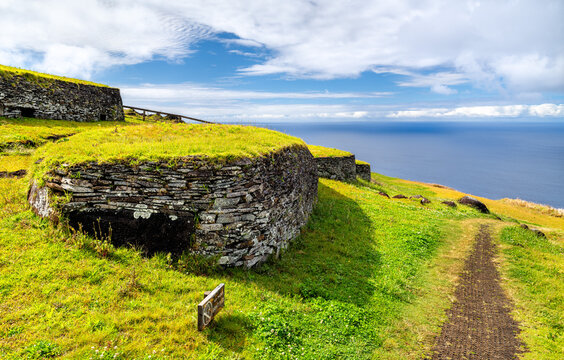 Ancient stone structures at the Orongo ceremonial village on Easter Island, Chile, with the blue Pacific Ocean in the background.