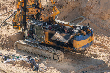Fototapeta premium Large tracked excavator engaged in earthmoving activities, yellow and blue painted machinery, sandy open excavation site with steep slope, dusty environment, tools scattered around, heavy use tracks