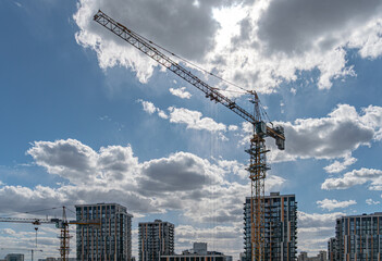 Fototapeta premium Construction site featuring tower crane, high-rise buildings, dynamic sky, sunlight filtering through clouds, vibrant blue backdrop, industrial materials, modern architecture