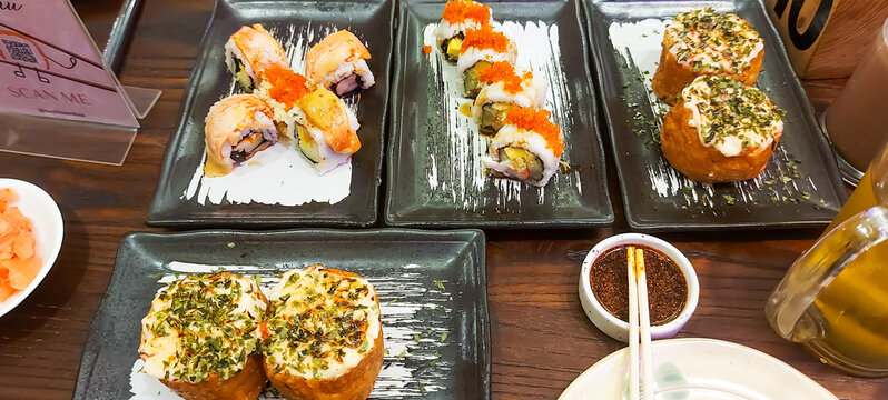 Delicious assortment of Japanese sushi rolls and creamy baked sushi served on black ceramic plates with soy sauce and chopsticks on a wooden dining table