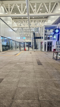 Empty concourse of a modern transit station featuring a high steel roof structure, tiled floors, and an elevator, representing advanced public infrastructure.
