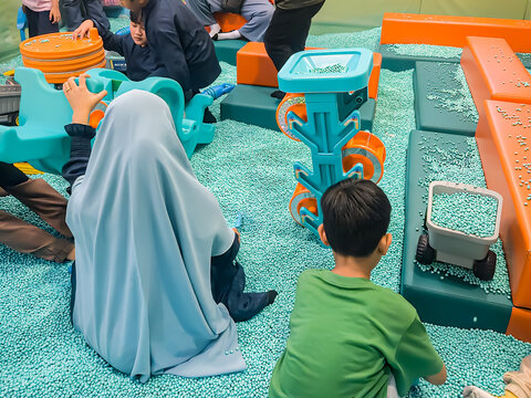 Candid moment of children and a mother in a hijab engaging in interactive sensory play with colorful granules and plastic toys at an indoor playground