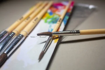 Fotobehang Schilderij Close up of artist wooden paintbrushes resting on a colorful blurred paint palette with a shallow depth of field  © prawira