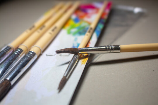 Close up of artist wooden paintbrushes resting on a colorful blurred paint palette with a shallow depth of field