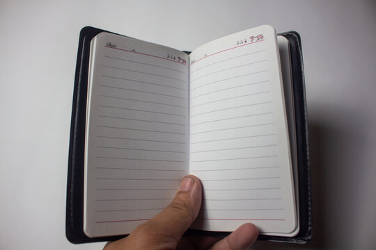 Hand holding an open blank lined notebook with a black cover against a white background, ready for writing, planning, or note-taking