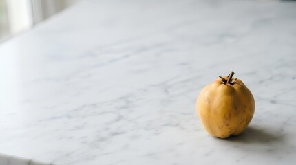 A single whole quince with subtle fuzz resting in the lower right corner of a large white marble surface, most of the frame left empty as negative space for seasonal fruit or artisanal food copy.