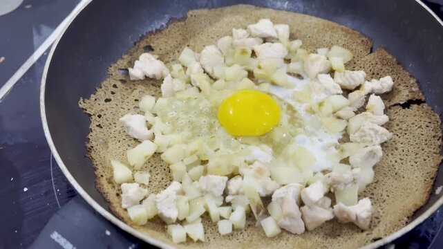 Buckwheat galette cooking in a frying pan with egg yolk chicken