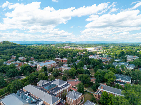 Charlottesville, Virginia, wide aerial drone view looking over the expansive University of Virginia campus and medical center complex, stretching toward rolling green hills under a bright sky 
