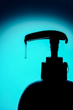 Liquid soap drop dripping from pump bottle dispenser in blue monochrome