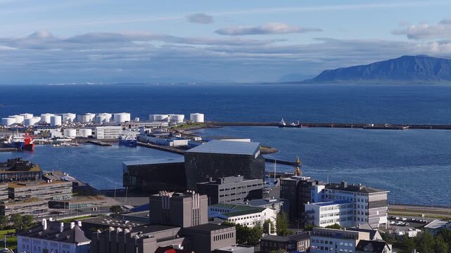 Aerial view of Reykjavik harbor in Iceland, fuel tanks, breakwater. Small ships move, cars and buses pass along the coastal road in daylight.