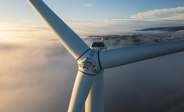 Aerial view of a wind turbine rotor emerging above morning fog, highlighting clean energy infrastructure in Loriol-sur-Drome, Auvergne-Rhone-Alpes, France.