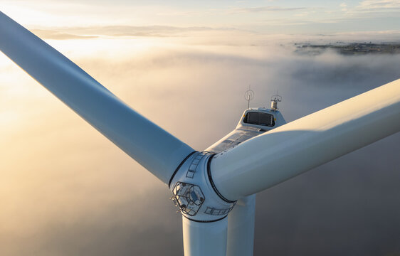 Aerial view of a wind turbine rotor emerging above morning fog, highlighting clean energy infrastructure in the countryside of Loriol-sur-Drome, Auvergne-Rhone-Alpes, France.