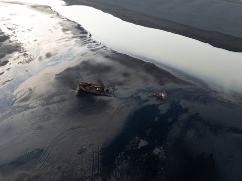 Aerial view of a rusted shipwreck resting on the dark volcanic sand of a beach in Iceland.