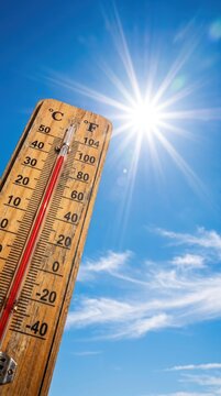 Close up of a wooden thermometer showing high temperatures against a bright blue summer sky with sun glare