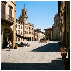 Fototapeta premium Sunny historic stone square with clock tower and outdoor cafe in Italian town