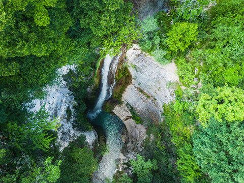 Aerial view of Chute de la Druise cascading into a turquoise pool surrounded by lush green forest and rocky cliffs in Plan-de-Baix, Auvergne-Rhone-Alpes, France.