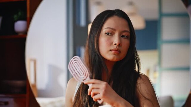 Asian woman combing long hair into round mirror. Closeup home self care beauty