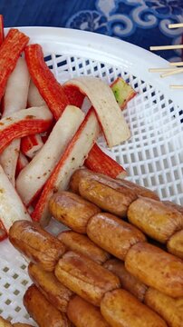 Assorted Street Food Skewers of Sausages and Fishballs on a Metal Grill