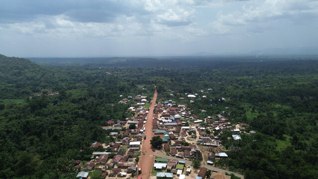 Aerial view of Gblede village near the lush green slopes of Afadjato Mountain with a dirt road running through the center and dense forest surroundings in Gblede, Volta Region, Ghana.