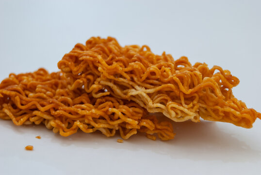 A high angle shot displaying a small tidy heap pile of crispy crushed instant noodle snack over a clean white surface backdrop.