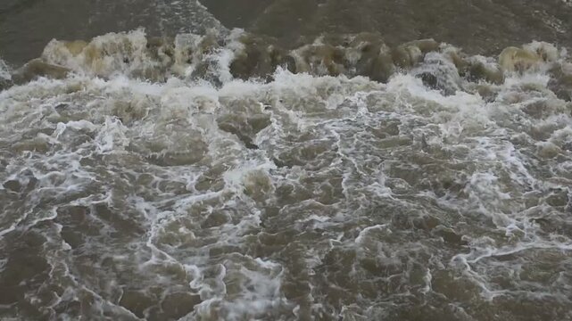 Waves crash onto wet, dark sand. Foam swirls, mixing with sea's rushing motion. Water churns, creating textured, frothy patterns. Beach edge is visible, showing tide's constant force