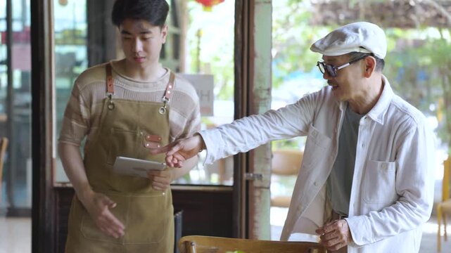 Family small business, senior cafe owner placing hiring sign on glass door, recruitment and expanding team concept in local coffee shop and restaurant. Cafe owner teaching barista about work process