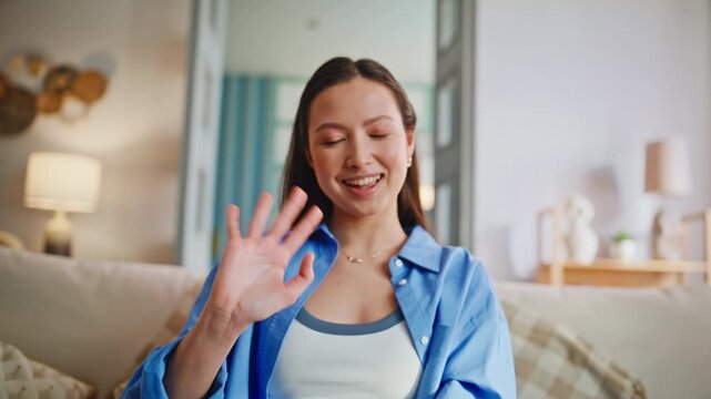 Vlogger waving hello talking webcam home. Closeup woman video call couch.