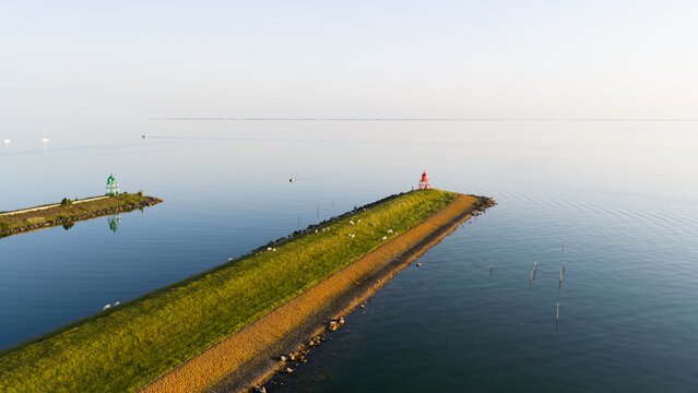 Aerial view of the harbor entrance with a red lighthouse on a grassy breakwater and a green lighthouse on the opposite pier in Stavoren, Friesland, Netherlands.