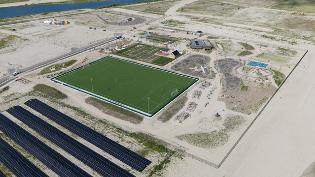 Aerial view of the Strandeiland recreational area featuring a soccer field, a pump track, and rows of solar panels in a developing urban landscape in Amsterdam, Noord-Holland, Netherlands.