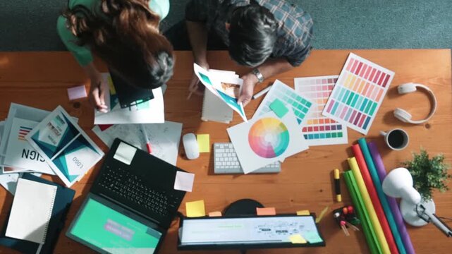 Top down view of smart designer helping manager choosing color from colored palettes. Aerial view of businessman working together and planning together while looking at logo from laptop. Symposium.