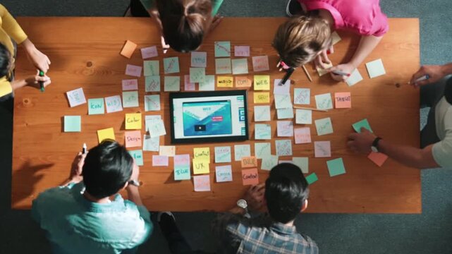 Top down view of programmer brainstorming and planning about web design while looking at tablet wireframe prototype. Aerial view of skilled developer team talking about digital application. Symposium.