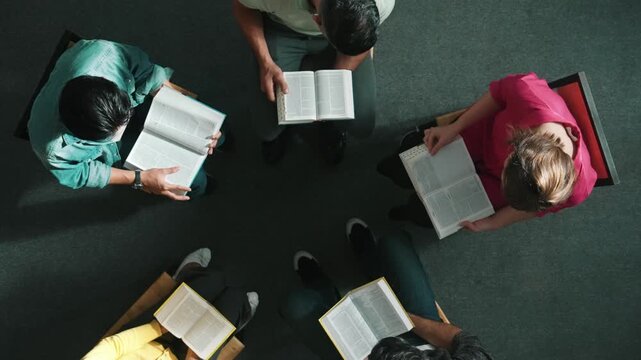 Top down view of prayer reading at bible book and sitting in circle with bible book on laps. Aerial view of diverse people looking at book while studying with faith, trust and hope, calm. Symposium.