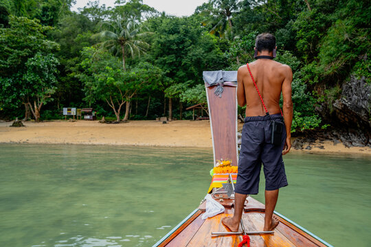 Man navigating longtail boat towards tropical beach in thailand