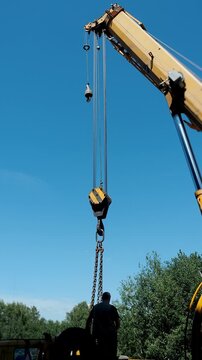 Mobile crane with hook block and rigger preparing for heavy lifting at a construction site. Industrial lifting equipment, construction engineering and safe load handling.