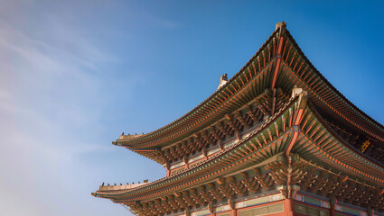 Obraz premium Ornate roof of a traditional Korean palace with painted dancheong eaves against a clear blue sky, authentic Korean heritage architecture and culture concept, editorial travel shot with copy space