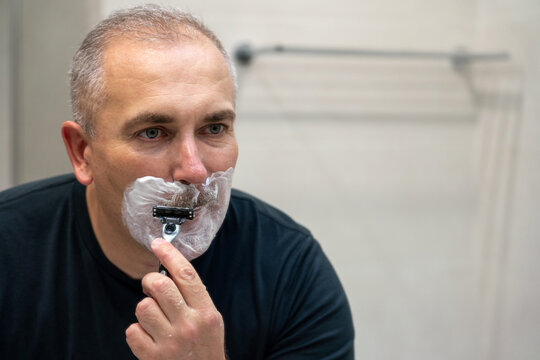 Man shaving with razor using foam in bathroom in the morning
