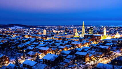 Obraz premium Winter Cityscape at Dusk: A breathtaking aerial view of a snow-covered city illuminated by the soft glow of twilight, showcasing a panorama of twinkling lights against a deep blue sky.