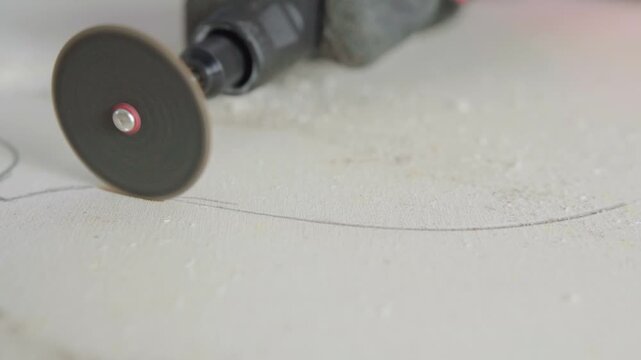 A close up view of a man using a rotary tool to create a groove in a white surface in slow motion.