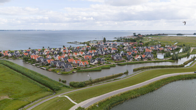Aerial view of EuroParcs Resort Port of Amsterdam featuring modern vacation homes nestled along the water, surrounded by green dikes and the Markermeer lake in Uitdam, Noord-Holland, Netherlands.